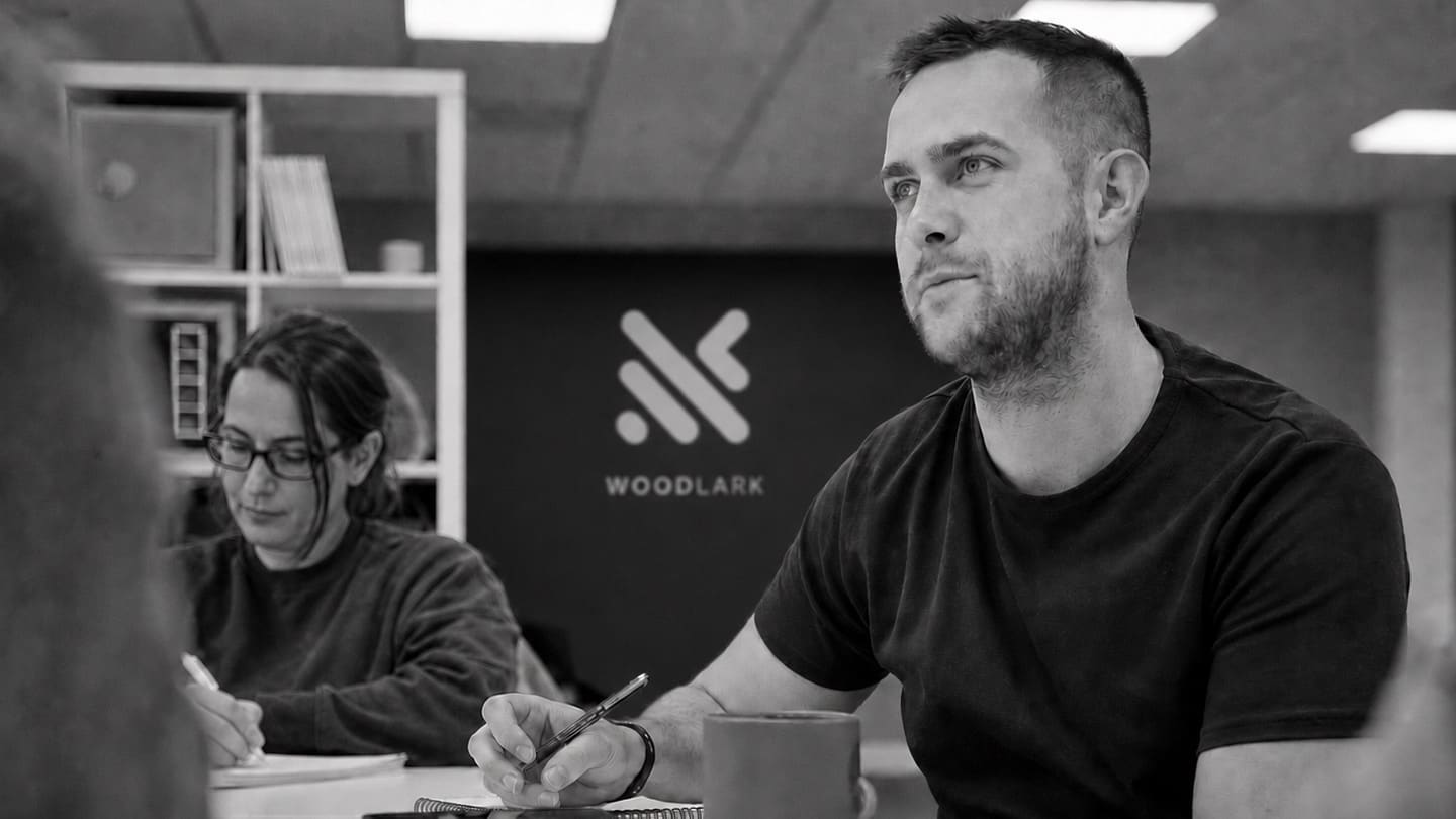 A working session around a table, with the Woodlark logo on the wall behind.